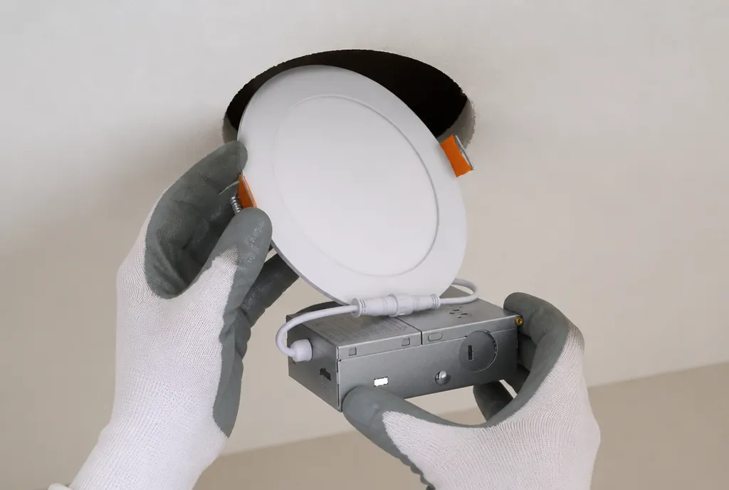 A slim zPLC downlight and its junction box being fitted into a ceiling cut-out